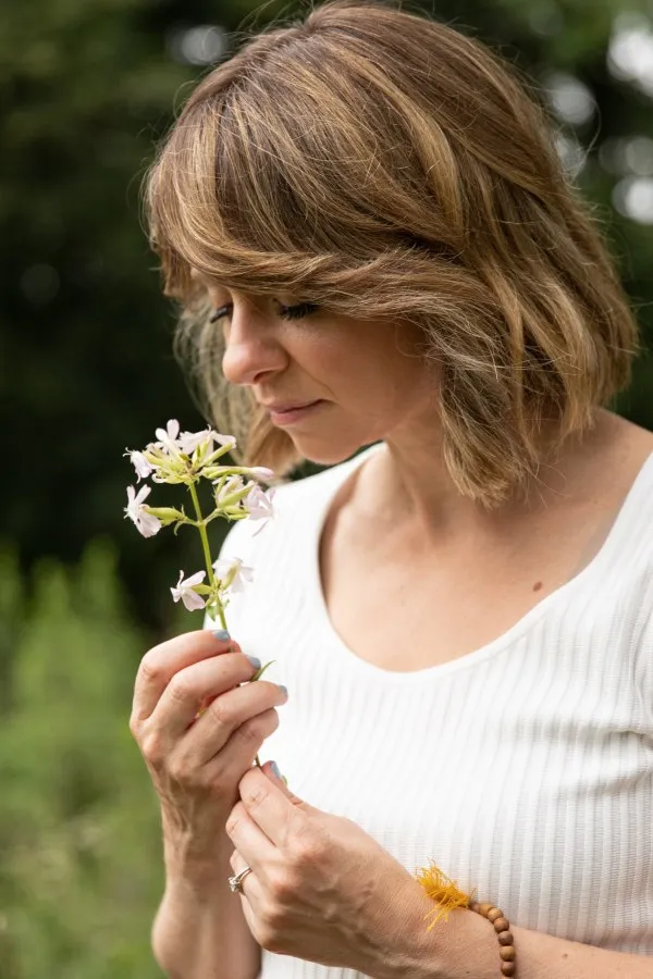Yael Shy smelling a small white flower